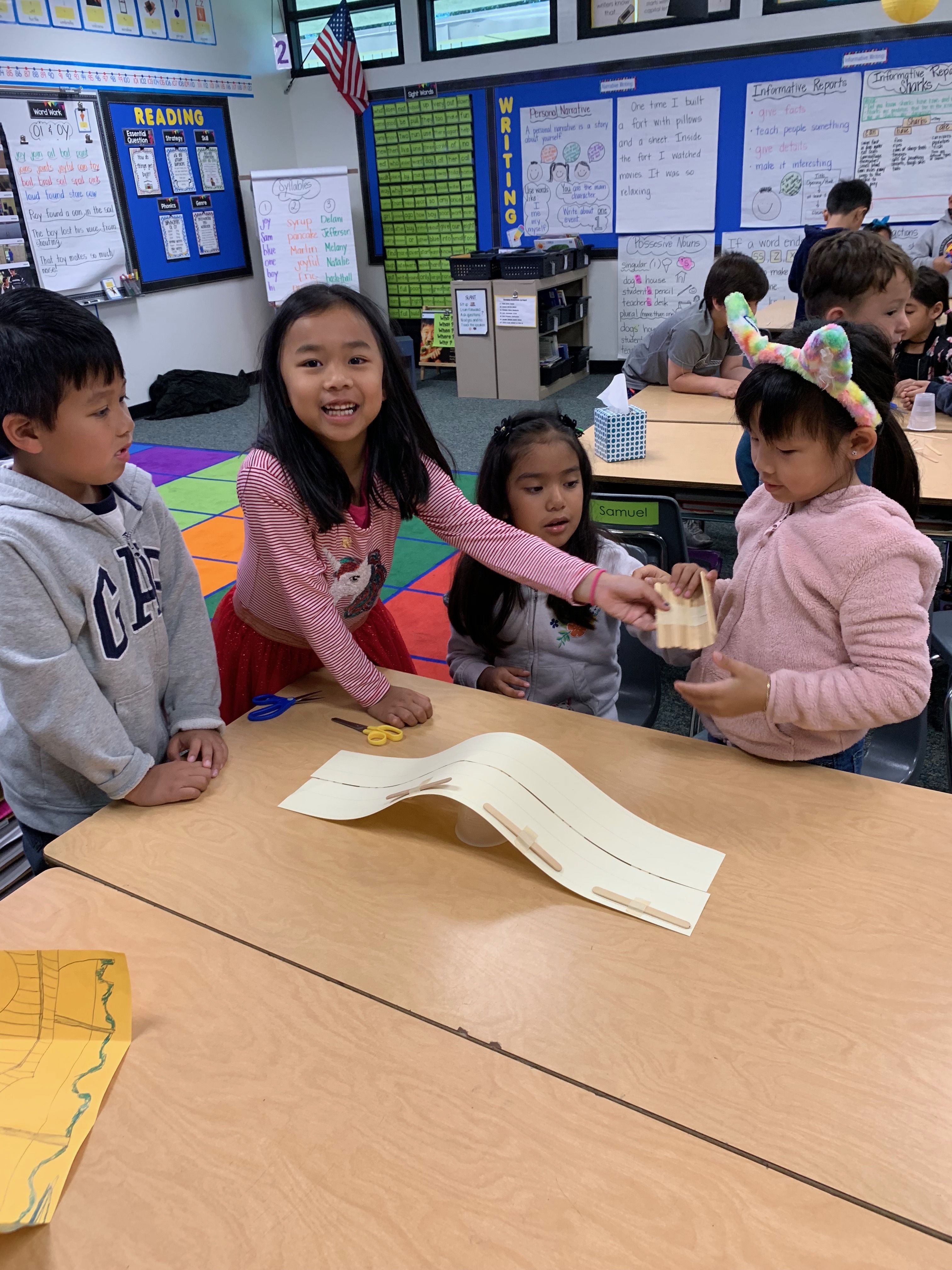 Students building a bridge out of popsicle sticks, a cup, and tape.